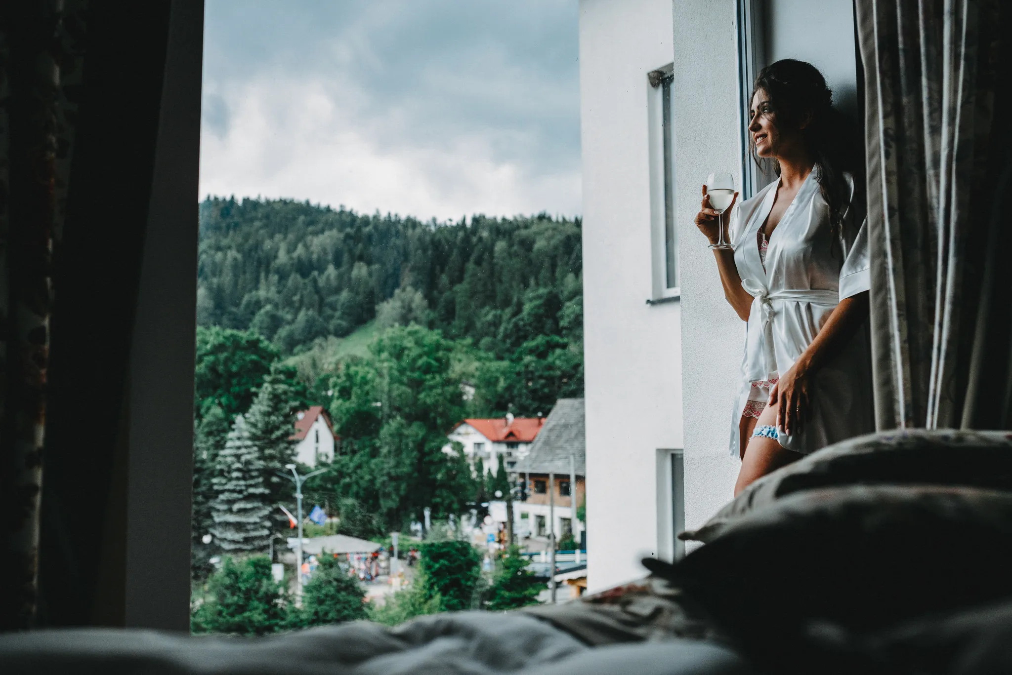 pani loda na przygotowaniach w szlafroku z podwiazka na nodze oraz kieliszkiem wina spoglada na gory. fotograf slubny szczyrk
